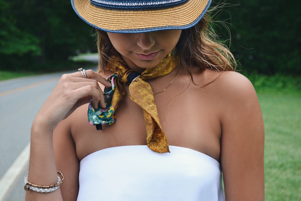 Girl looking down, wearing a straw fedora hat with blue trim and a yellow floral neck tie.