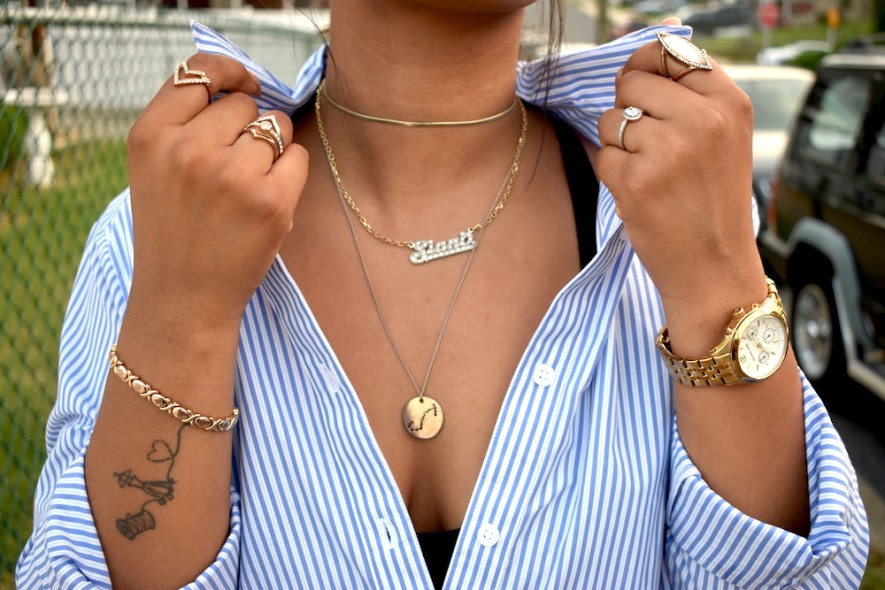 Close up view of a female wearing multiple layers of minimalistic jewelry on the fingers, neck, and wrists. 