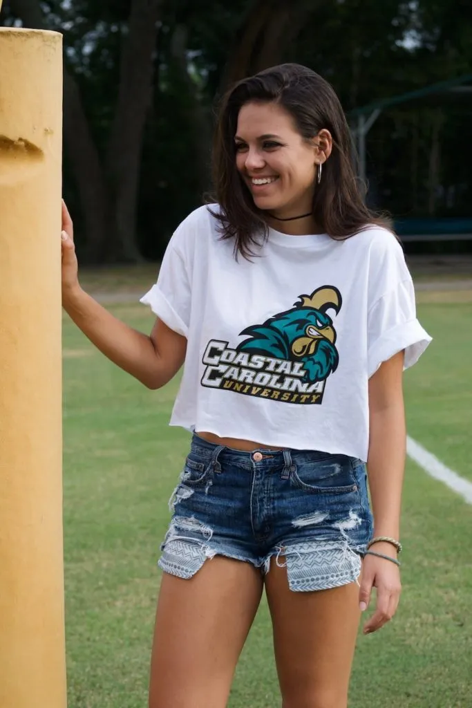 Girl in cropped college t-shirt and jean shorts on football field.