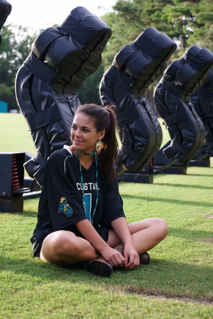 Girl in oversized jersey for tailgate, sitting in front of football gear. 