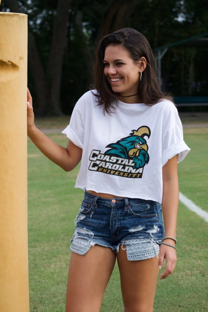 Girl in cropped college t-shirt and jean shorts on football field.