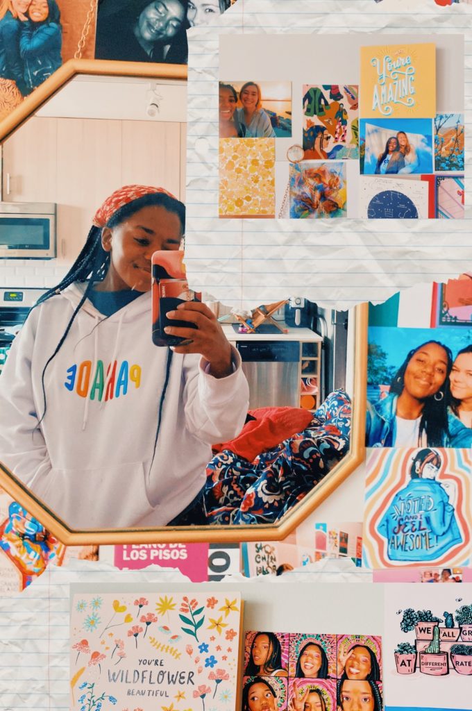 Tamia18 from Instagram standing in front of the mirror for a selfie with a gallery wall using Hallmark cards around the mirror. 